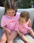 Two children in pink shirts sitting in Small But Sassy