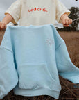 Light blue hoodie with a logo held by a person in a field