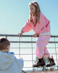 Child in pink outfit climbing a fence with another child in the foreground.