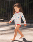 Young girl in a colorful swimsuit walking on a pavement.