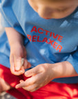 Child wearing a blue shirt with 'ACTIVE RELAXER' text, holding small stones.