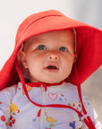 Baby wearing a colorful swimsuit and red sun hat with a blurred background