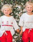 Two children wearing matching outfits with text and graphics against a leafy background