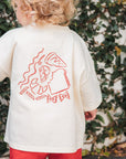 Child wearing a cream shirt with red graphics and red shorts standing in front of a green leafy background.
