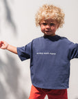 Child wearing a navy eat sleep snack repeat t-shirt with text and red shorts standing on a tiled floor.