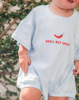 Child wearing a light blue t-shirt with 'Small But Spicy' text and red pepper graphic, standing outdoors.