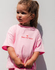 Child wearing small but sassy tee outdoors against a white wall.