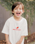 Child wearing a white t-shirt with small but spicy graphic and text, standing outdoors.
