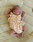 Newborn baby in a patterned outfit lying on a beige cushion
