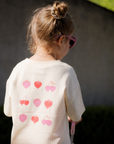 Child wearing a white shirt with pink heart patterns outdoors