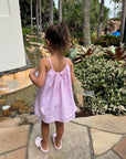Young girl in a pink dress standing on a stone path with garden and trees in the background