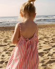 Young girl in a striped dress standing on a sandy beach looking at the ocean.