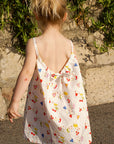 Child in a floral dress walking on a sidewalk with greenery in the background