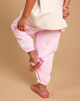 A child wearing an oversized cream t-shirt and light pink jogger pants, standing against a solid beige background.