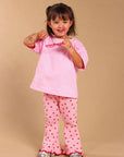 A young girl smiling and posing in a pink short-sleeve t-shirt and matching pink pants with small red star patterns, set against a solid beige studio background.