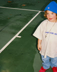 Child wearing a blue beanie and grey tee shirt on a tennis court