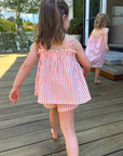 Two young girls in matching pink striped dresses walking on a wooden deck.