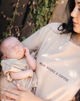 Woman holding a baby with 'Mum needs a coffee' shirt outdoors