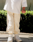 Person wearing beige pants and white shoes standing on a concrete surface with greenery in the background.