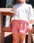 Child wearing a white top and red checkered shorts outdoors