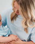 Woman holding a child wearing matching light blue shirts with text.
