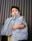 Child wearing a striped puffer vest and holding a skateboard against a dark background