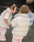 children in striped puffer jackets walking on a street.