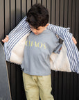 Child wearing a shirt with 'CHAOS' text, holding a striped jacket over their shoulders against a dark background.