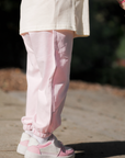 Person wearing light pink pants and white sneakers on a blurred outdoor background