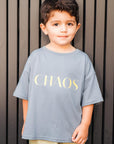 Child wearing a gray t-shirt with 'CHAOS' in yellow letters against a striped background