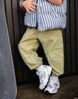 Person wearing a striped puffer and light green pants, and white sneakers with a skateboard.