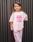Child wearing a pink outfit with a graphic design against a dark vertical panel background