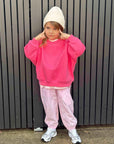 Child wearing a pink outfit with a white beanie against a dark vertical panel background