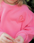 Person wearing a pink sweatshirt with a heart design outdoors