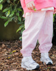 Person wearing a pink outfit with white shoes standing on mulch with greenery in the background