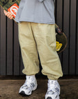 Person wearing olive pants and white sneakers holding a skateboard against a dark background