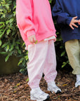 Two children wearing colorful outfits standing on mulch with greenery in the background