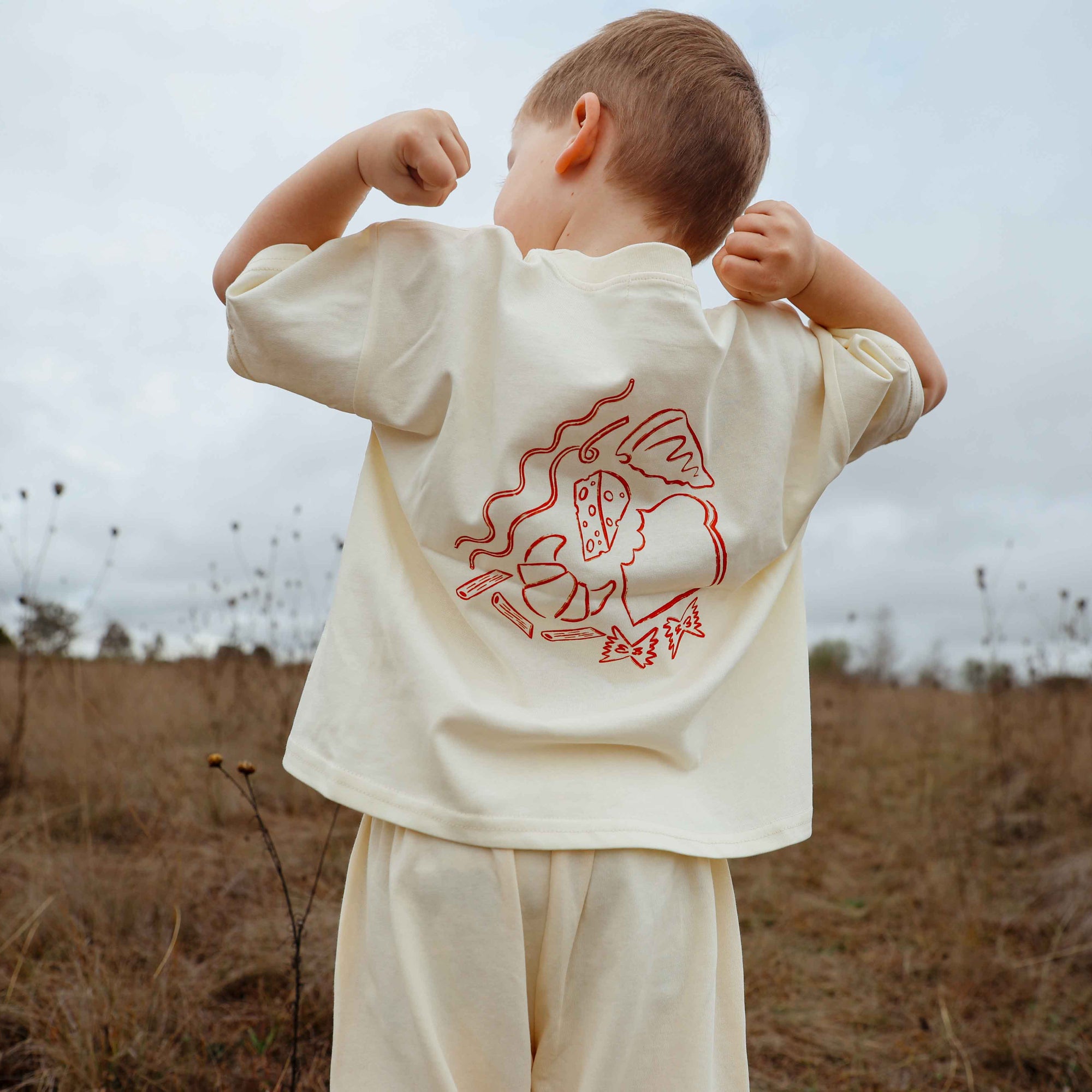 Child wearing a cream t-shirt with a red graphic design outdoors