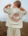Child wearing a cream t-shirt with a red graphic design outdoors