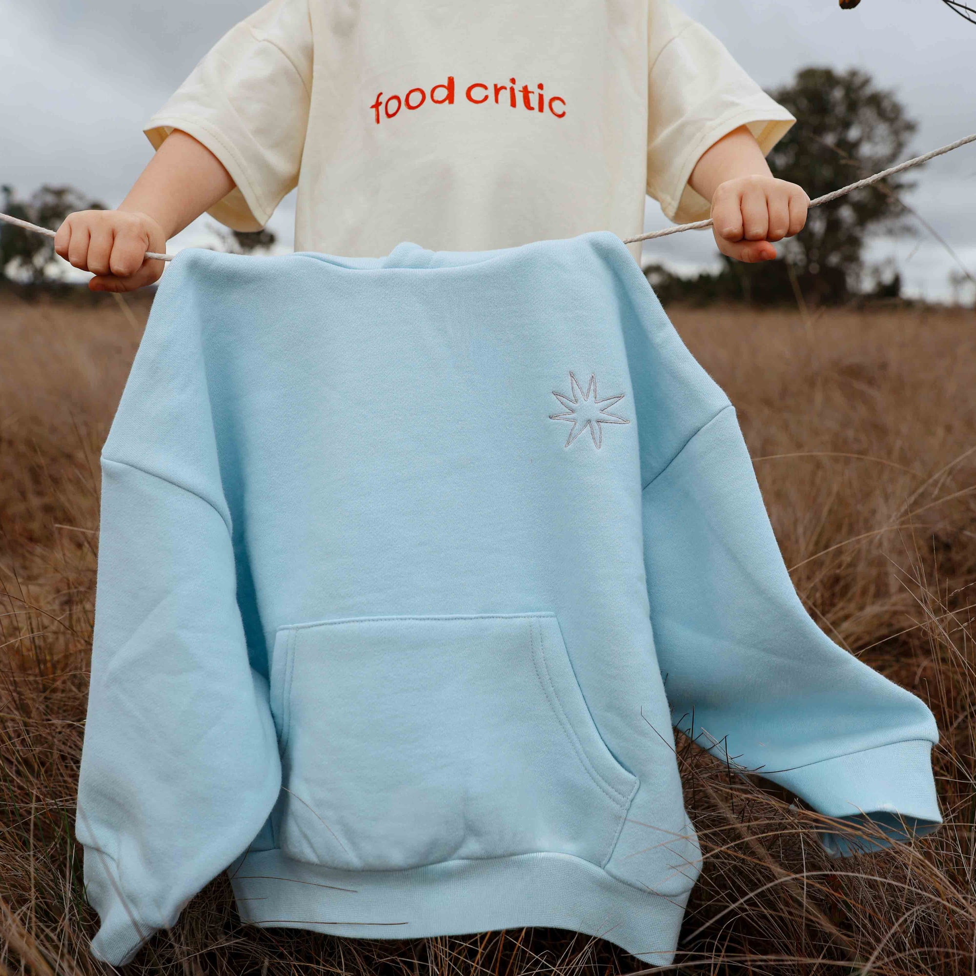Light blue hoodie with a logo held by a person in a field