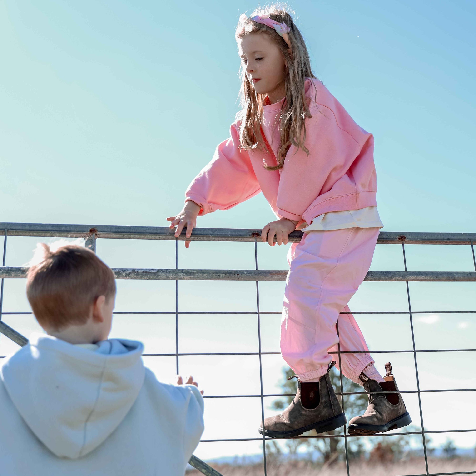 Child in pink outfit climbing a fence with another child in the foreground.