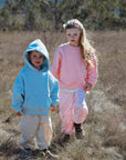 Two children in colorful outfits walking through a dry, open field with trees in the background.
