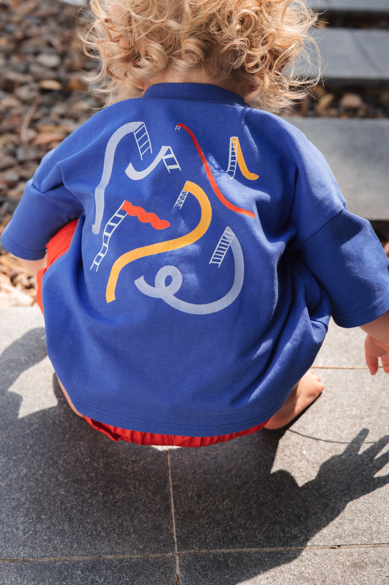 Child wearing a blue jacket with colorful designs on the back, standing on a stone surface.