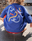Child wearing a blue jacket with colorful designs on the back, standing on a stone surface.