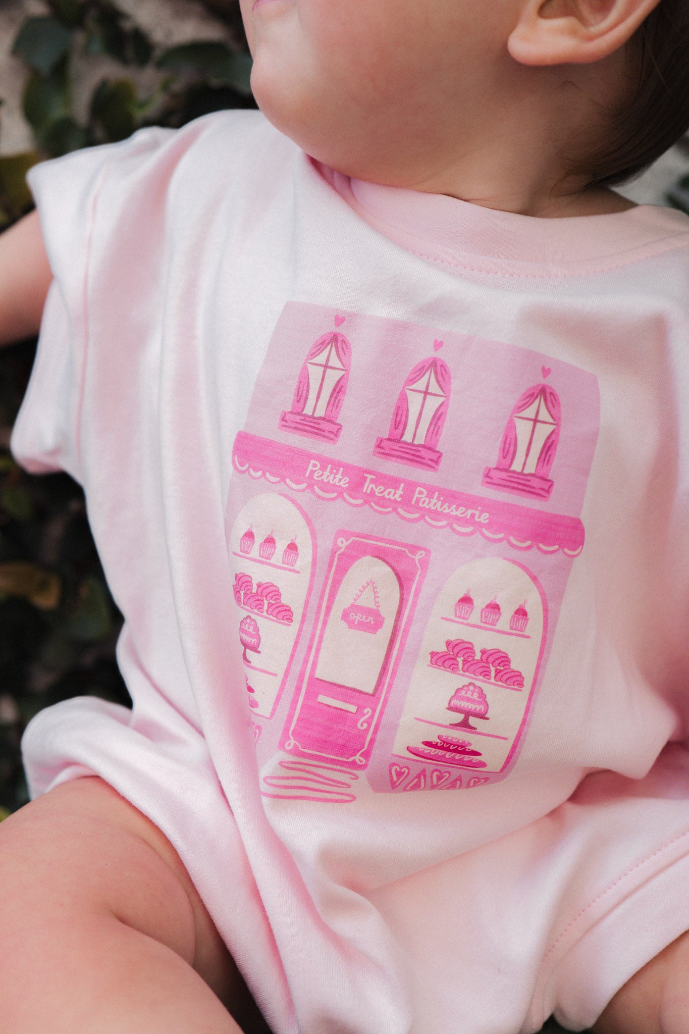Baby wearing a pink onesie with a petite treat patisserie design.