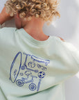 boy wearing a light green t-shirt with blue illustrations of children's toys on a white background