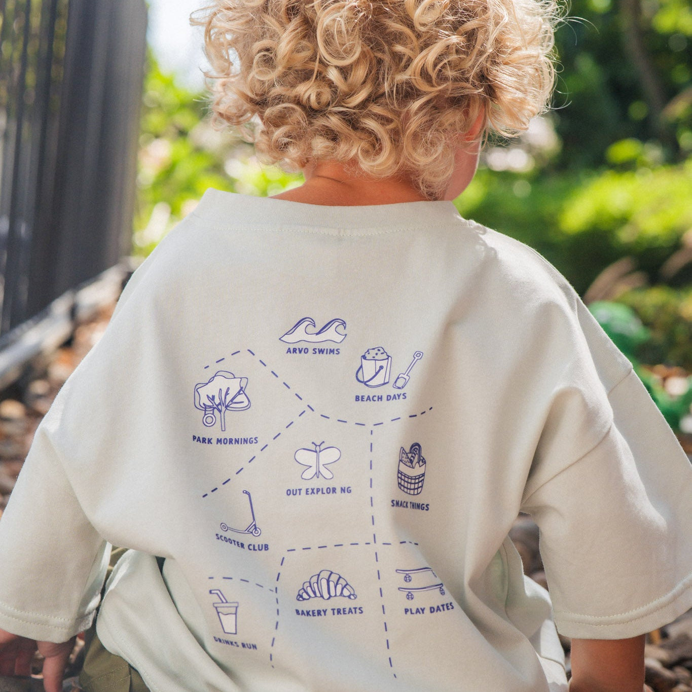 Child wearing a sky-colored shirt with graphics, sitting on rocks outdoors.
