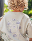 Child wearing a sky-colored shirt with graphics, sitting on rocks outdoors.