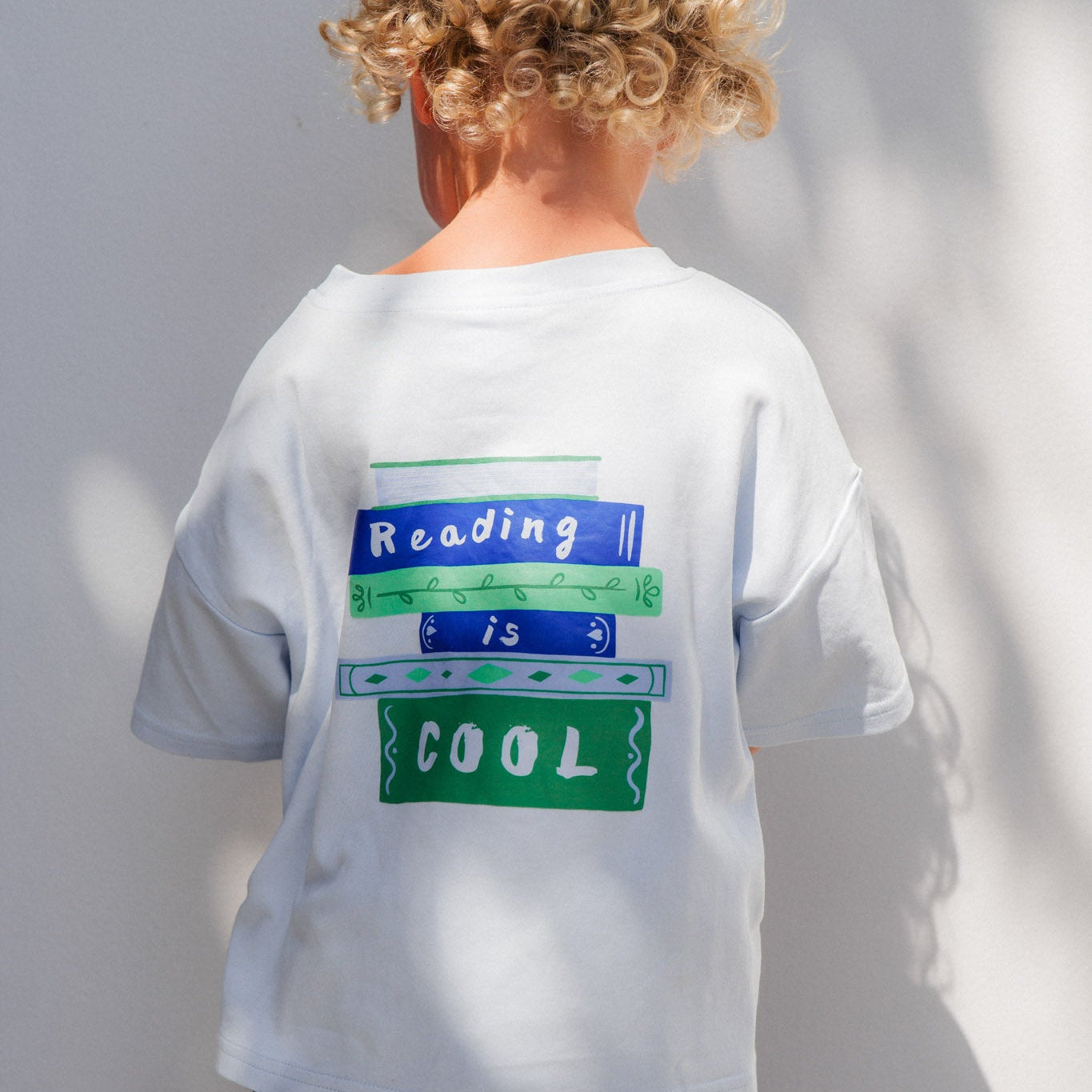 Child wearing a white t-shirt with text on the back, standing against a plain background