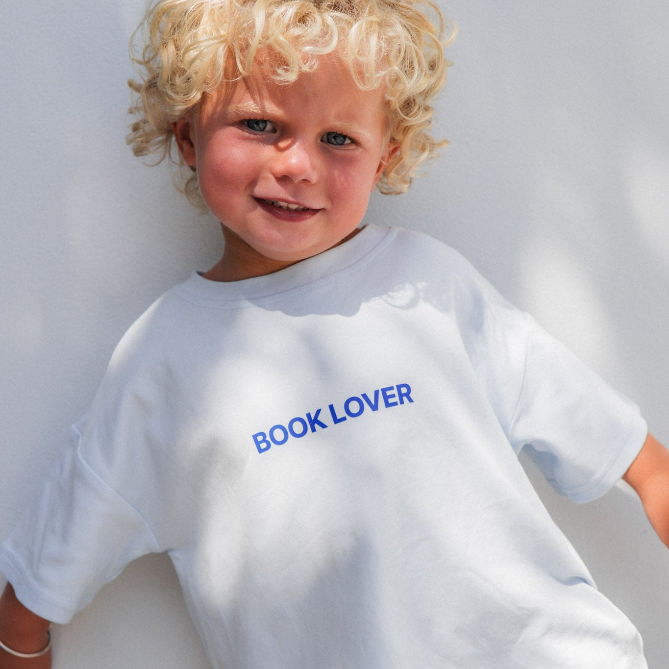 Child wearing a white t-shirt with 'BOOK LOVER' text on a light gray background